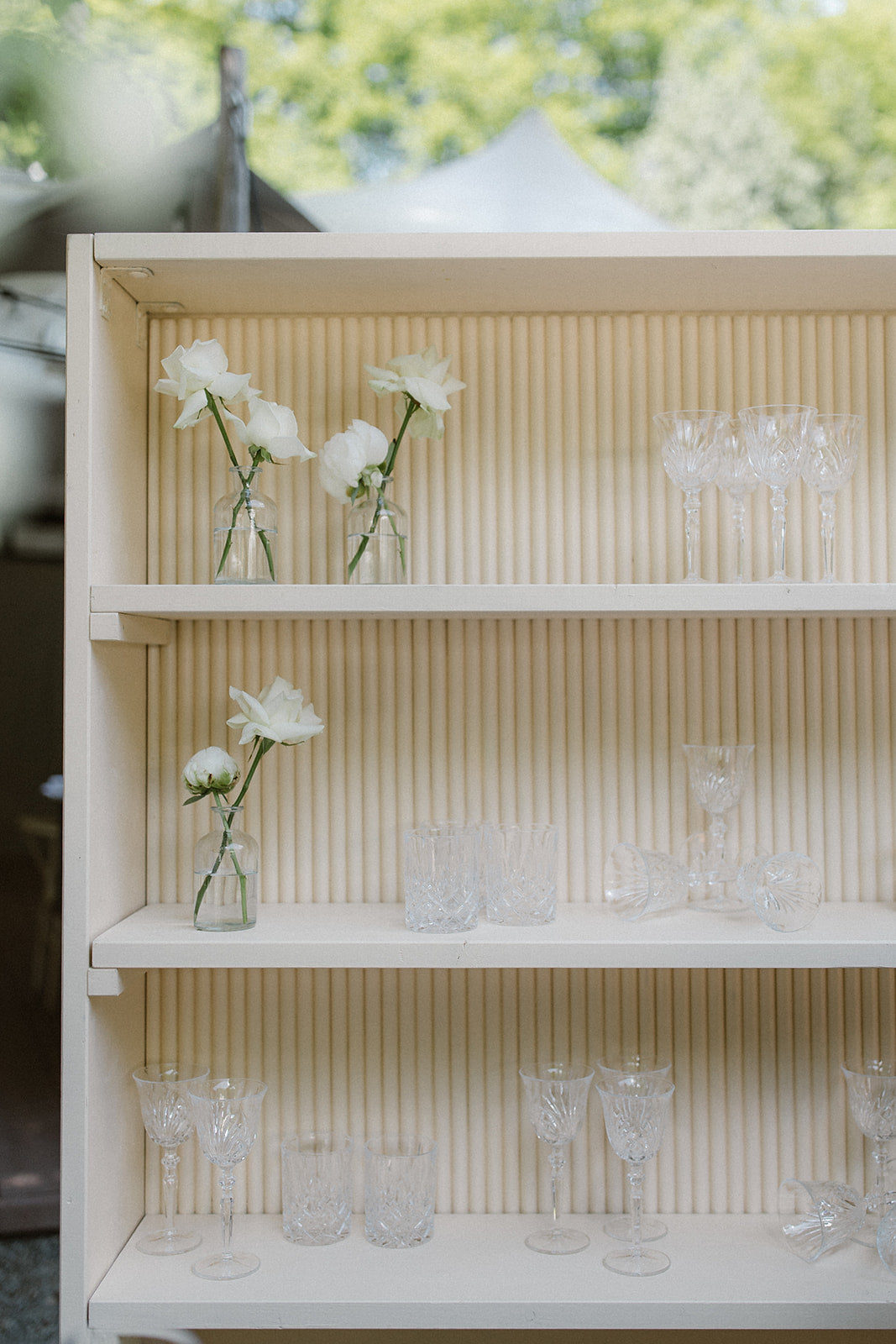 Beige Bar mit Kristallgläsern und weißen Blumen in kleinen Vasen. Dieses stilvolle beige Bar für eine Hochzeit ist mit eleganten Kristallgläsern und weißen Blumen in zarten Vasen dekoriert. Die schlichte, aber elegante Anordnung sorgt für eine harmonische und romantische Atmosphäre auf der Hochzeitsfeier.