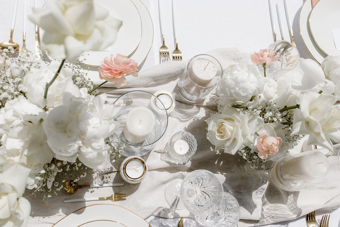 DIY-Hochzeitstisch mit weißen und rosa Blumen, Kerzen und Kristallgläsern in eleganter Anordnung. Diese elegante Hochzeitsdekoration kombiniert weiße und zartrosa Blumenarrangements mit Kerzen und feinem Kristall. Die harmonische Anordnung und die goldenen Akzente schaffen eine luxuriöse und romantische Atmosphäre auf dem Tisch. Perfekt für eine stilvolle Feier im Freien.
