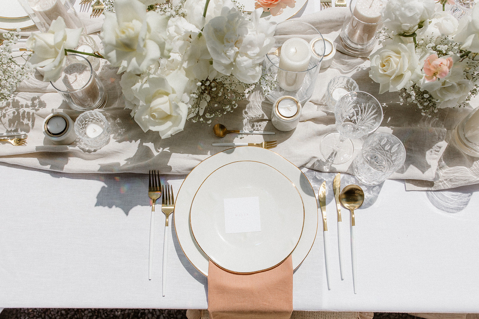 DIY-Hochzeitsdekoration mit weißen Blumengestecken, goldenen Besteckteilen und einer roséfarbenen Serviette auf dem Gedeck. Diese elegante Hochzeitstischdekoration besticht durch weiße Blumenarrangements, goldene Besteckteile und feine Kristallgläser. Eine zarte rosafarbene Serviette rundet das minimalistische Gedeck ab und verleiht dem Tisch eine romantisch-luxuriöse Note.