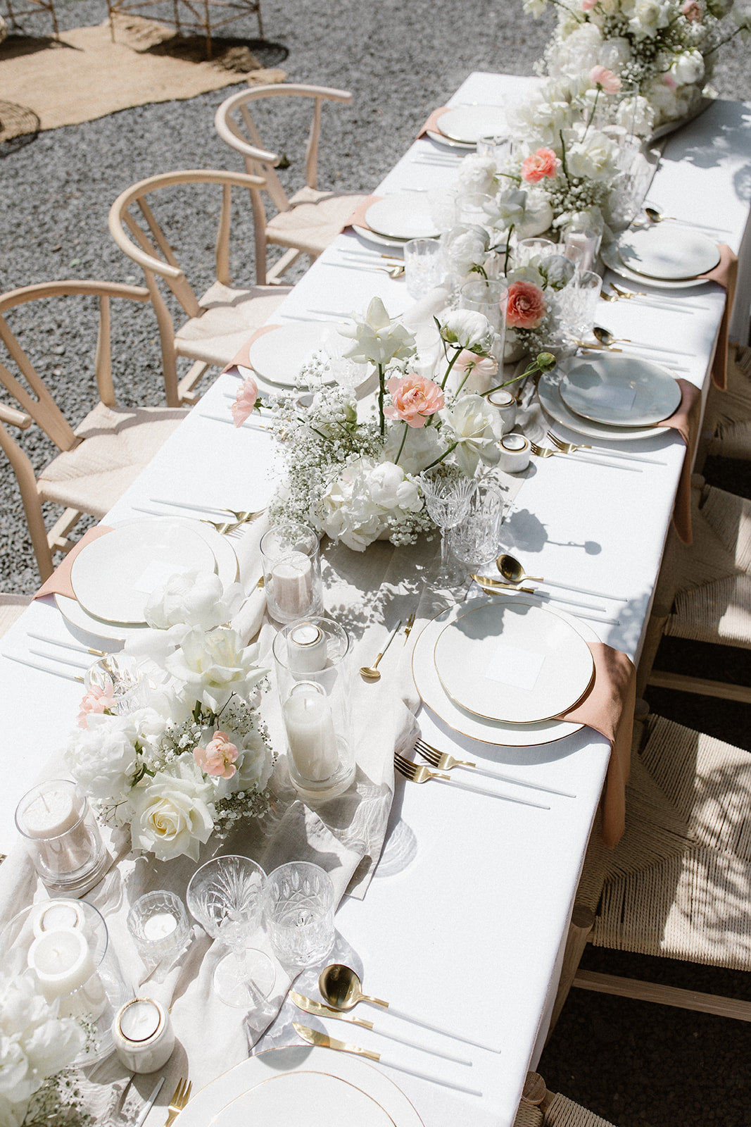 Lange Hochzeitstafel im Freien, dekoriert mit weißen und rosa Blumenarrangements sowie goldenen Akzenten. Diese festlich dekorierte Hochzeitstafel im Freien beeindruckt durch eine elegante Blumengestaltung in Weiß und Rosa sowie dezente goldene Akzente. Die harmonische Tischdekoration verleiht der Feier eine luxuriöse und romantische Atmosphäre unter freiem Himmel.