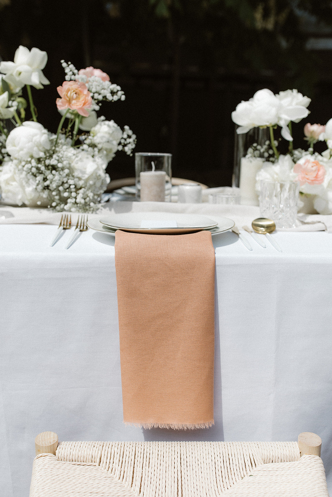 Hochzeitstisch mit rosa Serviette, weißen Blumen und romantischen Dekorationselementen. Diese minimalistische Hochzeitstafel besticht durch eine dezente rosa Serviette auf dem Gedeck, kombiniert mit weißen Blumenarrangements und schlichten Dekorationselementen. Die klare und elegante Gestaltung sorgt für eine moderne und romantische Atmosphäre.