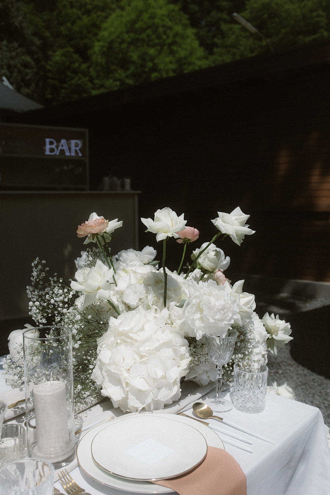 Hochzeitstisch mit opulenten weißen Rosen, Hortensien und dezenten rosa Akzenten. Diese romantische Hochzeitsdekoration kombiniert üppige weiße Rosen und Hortensien mit zarten rosa Akzenten. Die elegante Blumendekoration sorgt für ein luxuriöses und einladendes Ambiente auf dem festlich gedeckten Hochzeitstisch. Ideal für eine stilvolle Outdoor-Hochzeit.