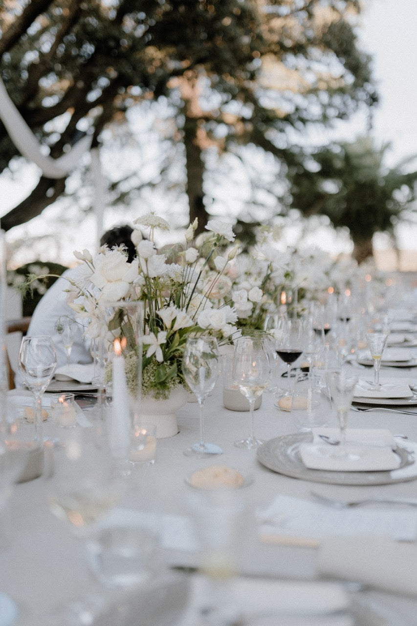  Stilvolle, elegante Hochzeitstafel im Freien mit weißen Blumenarrangements und Kerzen. Stilvoll gedeckte Hochzeitstafel im Freien mit weißen Blumenarrangements und Kerzen, die eine charmante und zeitlose Atmosphäre für die Hochzeitsfeier schaffen.