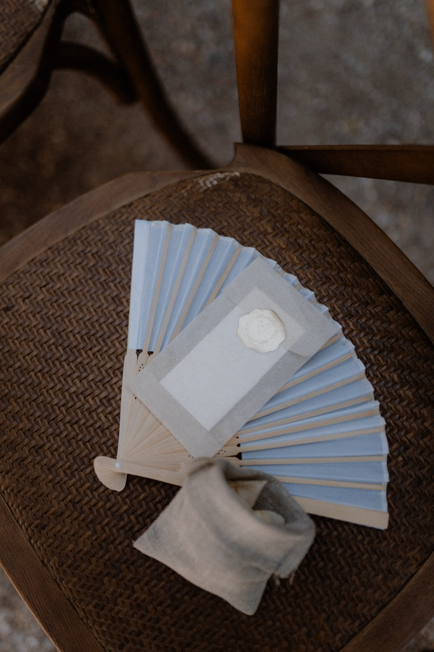 Schlichter Fächer auf einem rustikalen Stuhl bei einer Hochzeit. Ein charmantes Hochzeitsdetail mit einem schlichten Fächer, elegant platziert auf einem rustikalen Stuhl, passend für eine minimalistische und zeitlose Hochzeitsfeier.