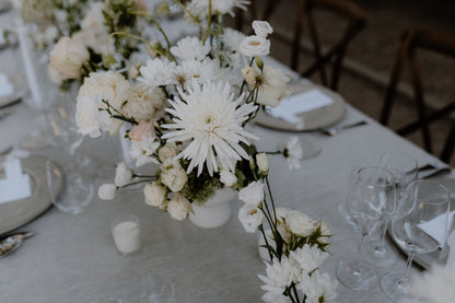 Schlichte und elegante Hochzeitstischdekoration mit weißen Blumen und dezenten Gläsern. Stilvolle Hochzeitstischdekoration mit weißen Blumenarrangements und zurückhaltendem Geschirr, ideal für eine zeitlose und charmante Hochzeitsfeier.