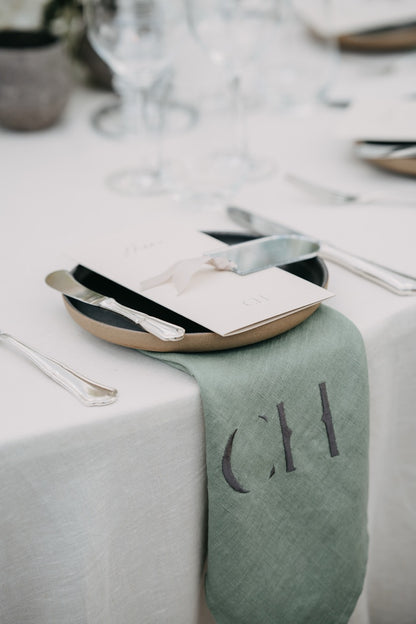 Ästhetische, personalisierte Serviette mit Monogramm und elegantes Tischgedeck bei einer luxuriösen Hochzeit. Dieses exklusive Tischgedeck besticht durch eine personalisierte Serviette mit Monogramm und edlem Besteck auf einem minimalistischen Teller. Die schlichte, elegante Tischdekoration fügt sich harmonisch in das luxuriöse Ambiente der Hochzeit ein und verleiht der Tafel eine individuelle Note. Perfekt für Paare, die Liebe zum Detail und Stil schätzen.