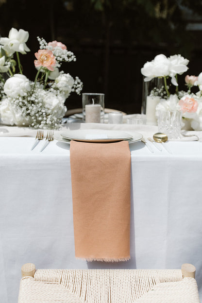 Hochzeitstisch mit rosa Serviette, weißen Blumen und romantischen Dekorationselementen. Diese minimalistische Hochzeitstafel besticht durch eine dezente rosa Serviette auf dem Gedeck, kombiniert mit weißen Blumenarrangements und schlichten Dekorationselementen. Die klare und elegante Gestaltung sorgt für eine moderne und romantische Atmosphäre.